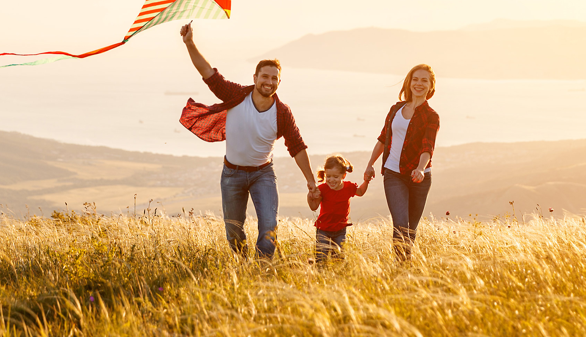 Family flying a kite on the top of a hill at sunset.