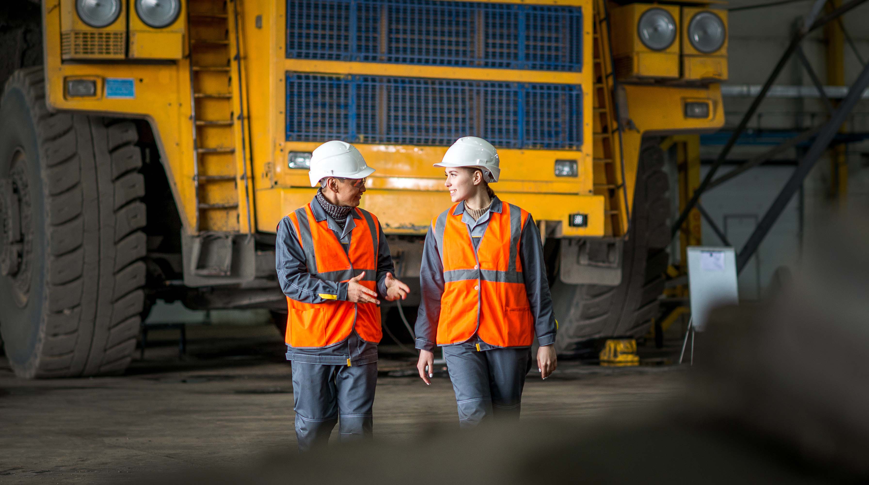 2 mine workers wearing protective equipment chatting in front of heavy machinery.