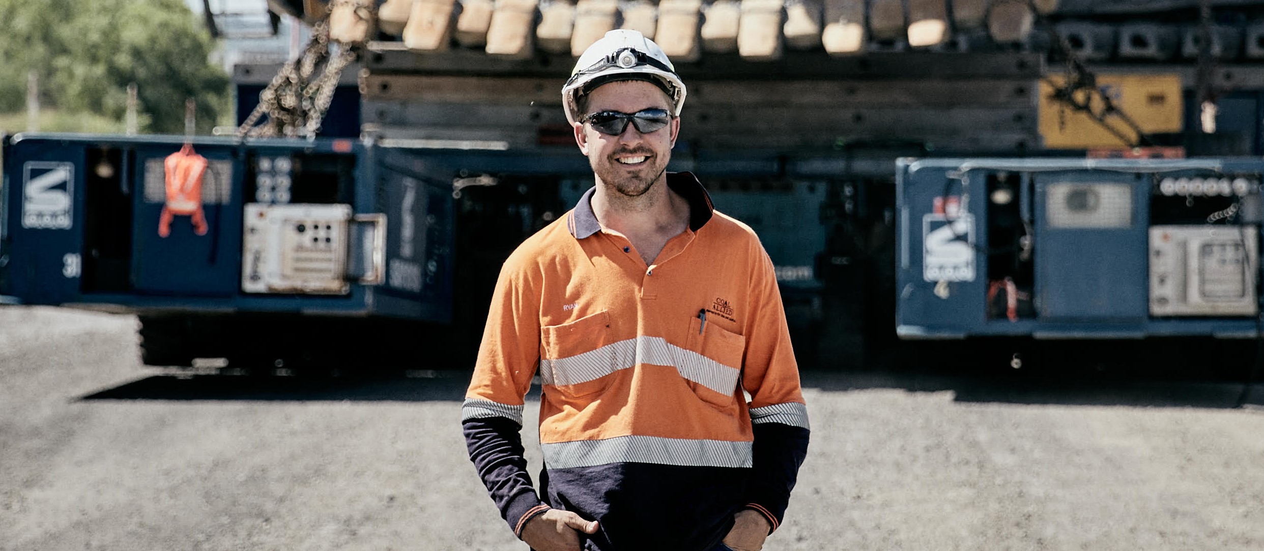 A coal miner standing in front of a mine truck smiling at the camera.