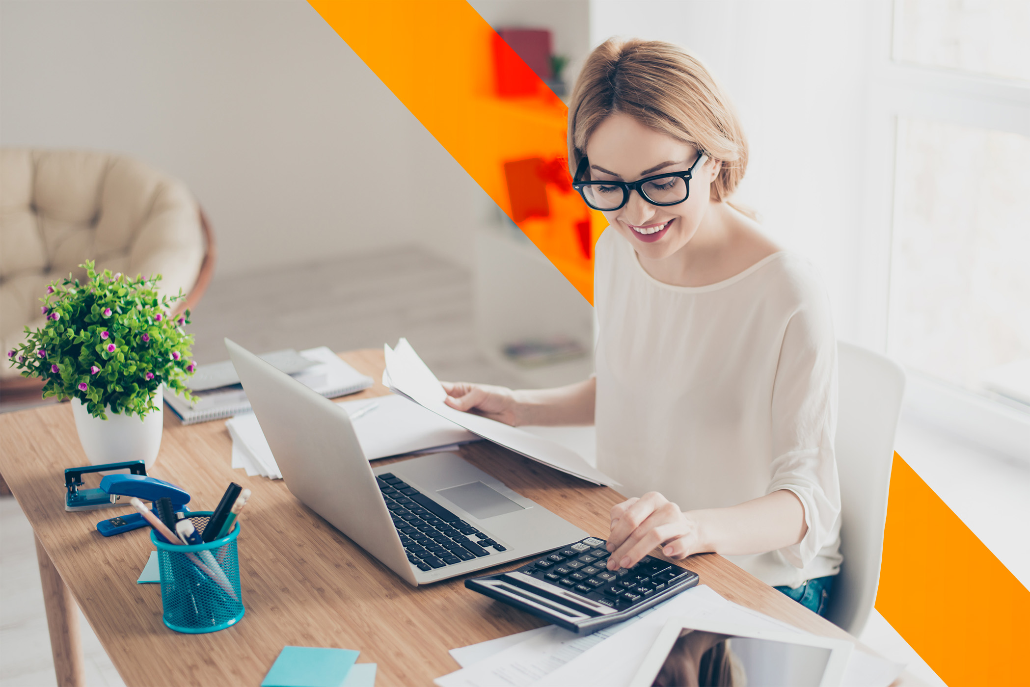 Young office worker wearing glasses using a laptop and a calculator.