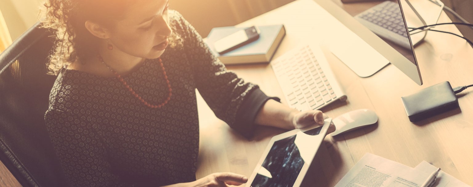 An office worker at her work station, using a mobile device.