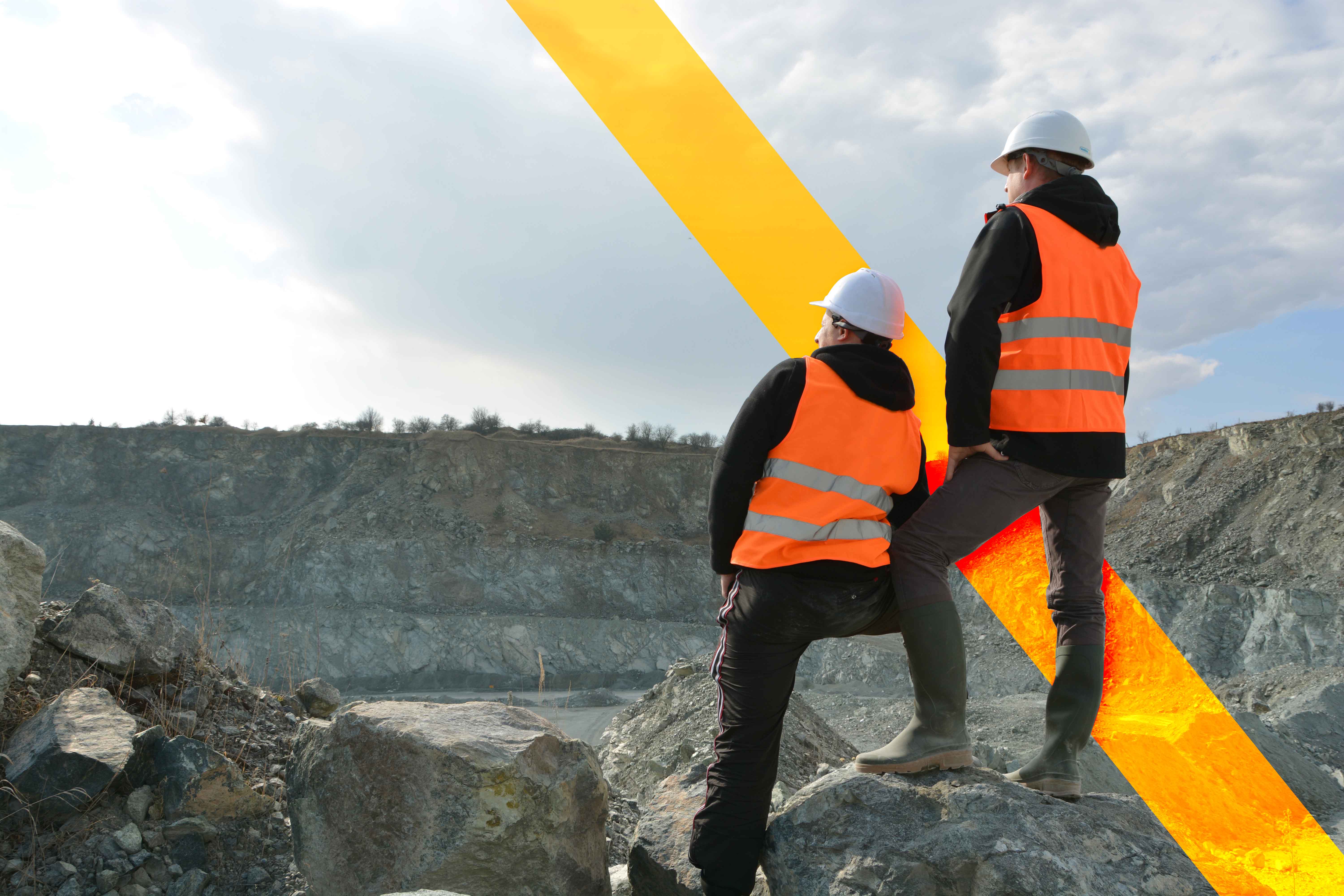 2 mine workers wearing protective equipment and looking over a mining pit.