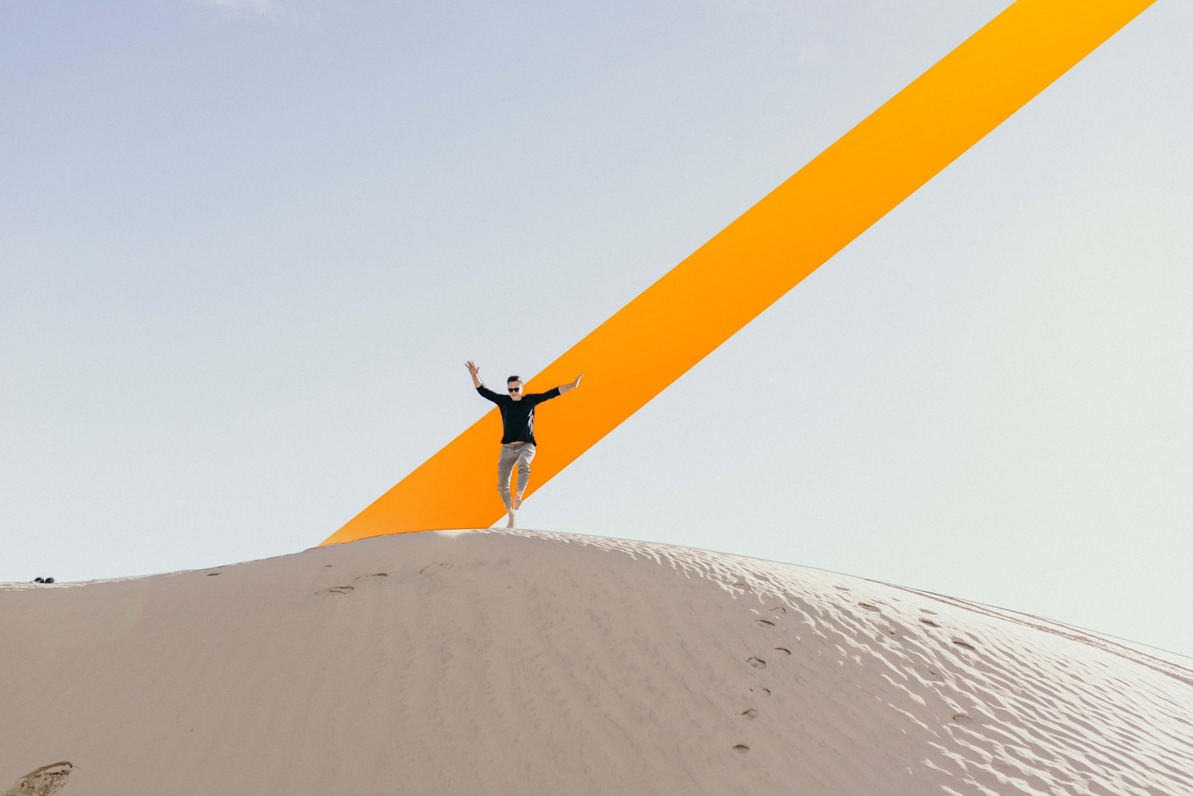 Man jumping and smiling in sand dunes.
