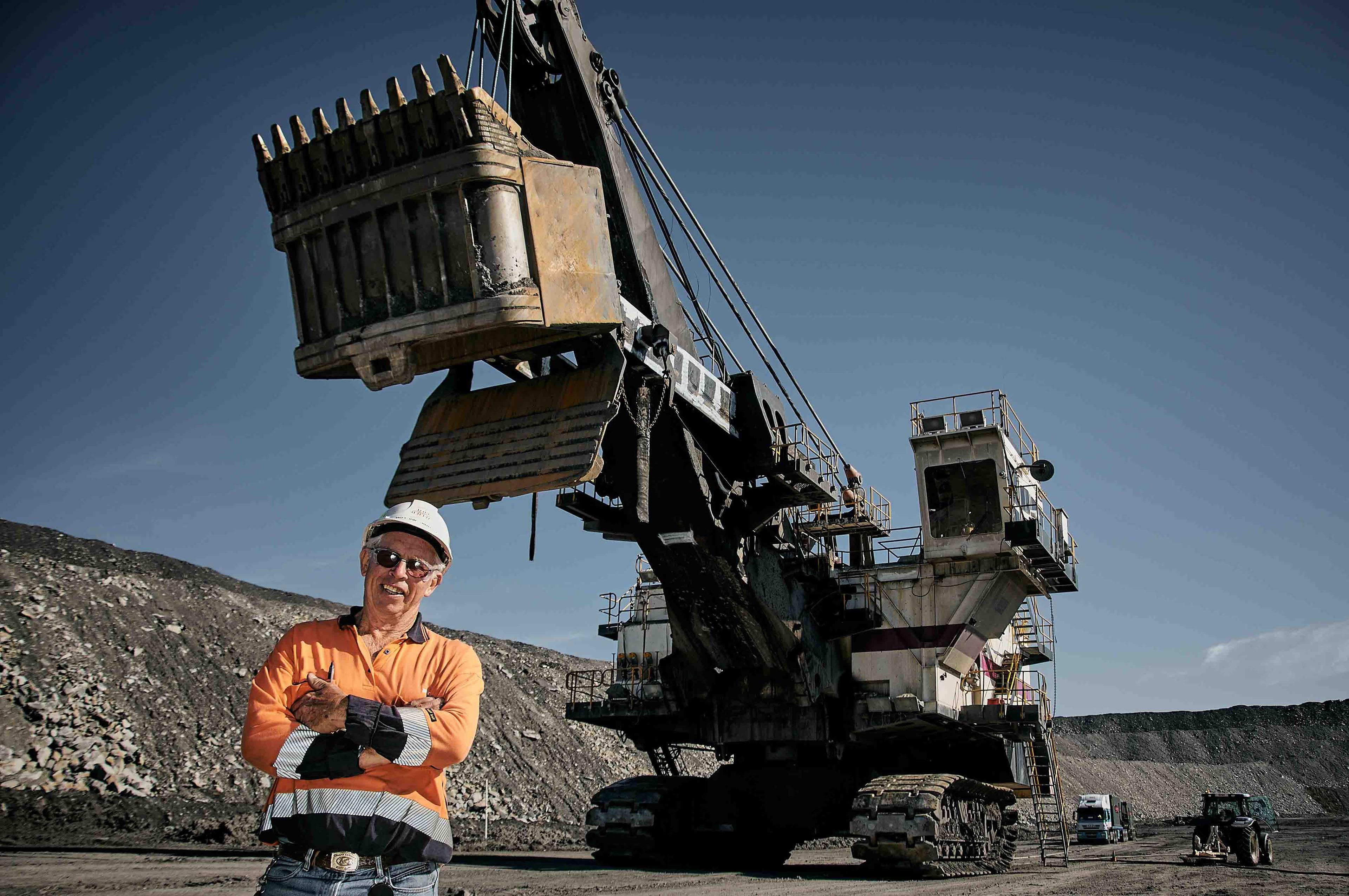 A smiling mine worker wearing protective equipment and standing in front of heavy machinery.